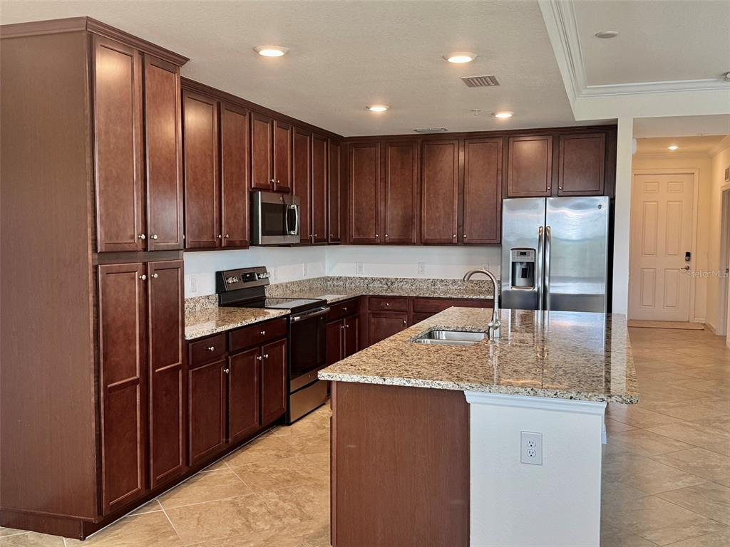 A kitchen features dark wood cabinets, granite countertops, stainless steel appliances, and a central island — 17118 VARDON TERRACE UNIT 303, BRADENTON, FL