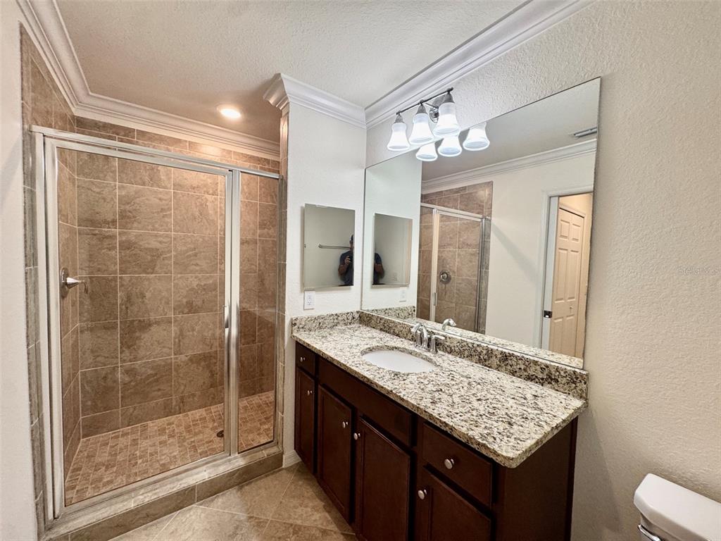 A bathroom features a walk-in tiled shower, a granite vanity, and a large wall mirror — 17118 VARDON TERRACE UNIT 303, BRADENTON, FL