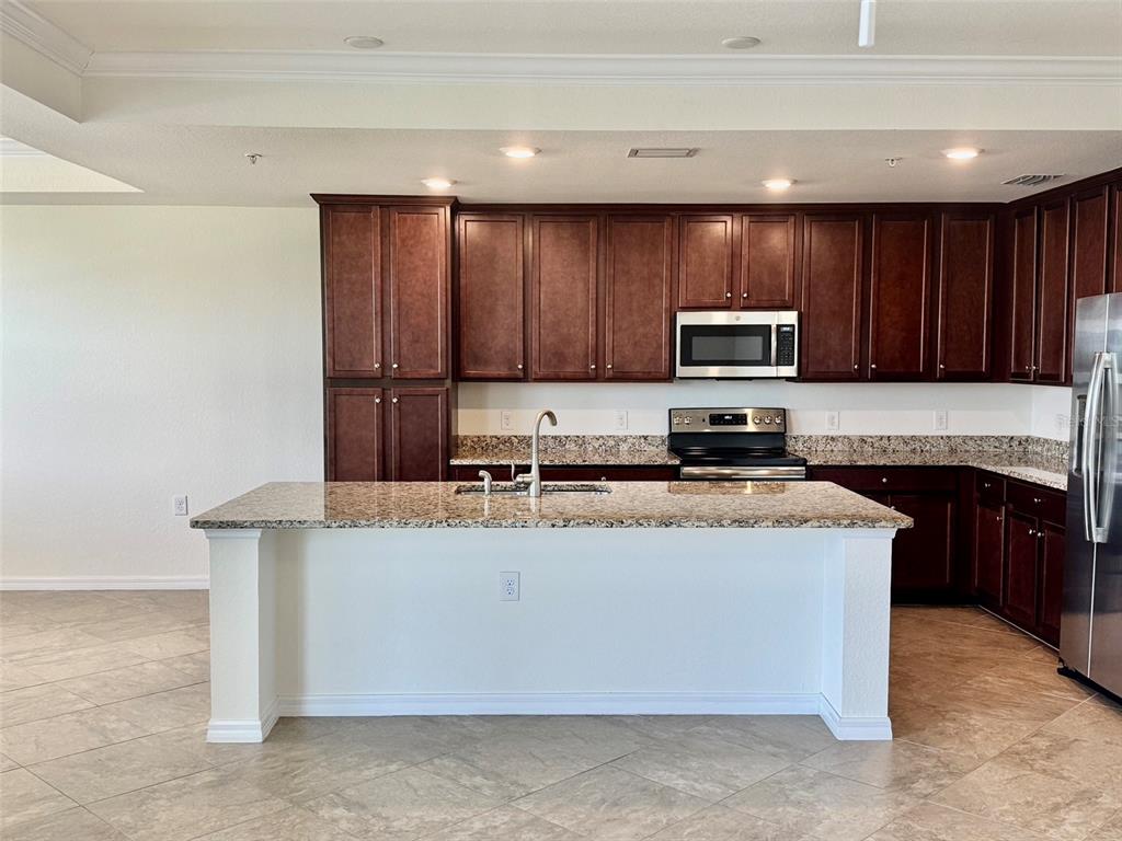 A kitchen features dark wood cabinets, granite countertops, a central island, and stainless steel appliances — 17118 VARDON TERRACE UNIT 303, BRADENTON, FL