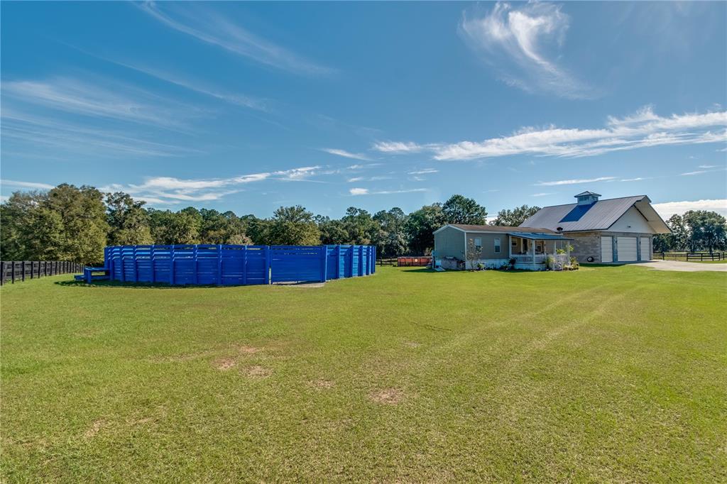 A large grassy yard features a blue circular horse pen, a mobile home, and a barn — 7787 NW 150TH AVENUE, MORRISTON, FL