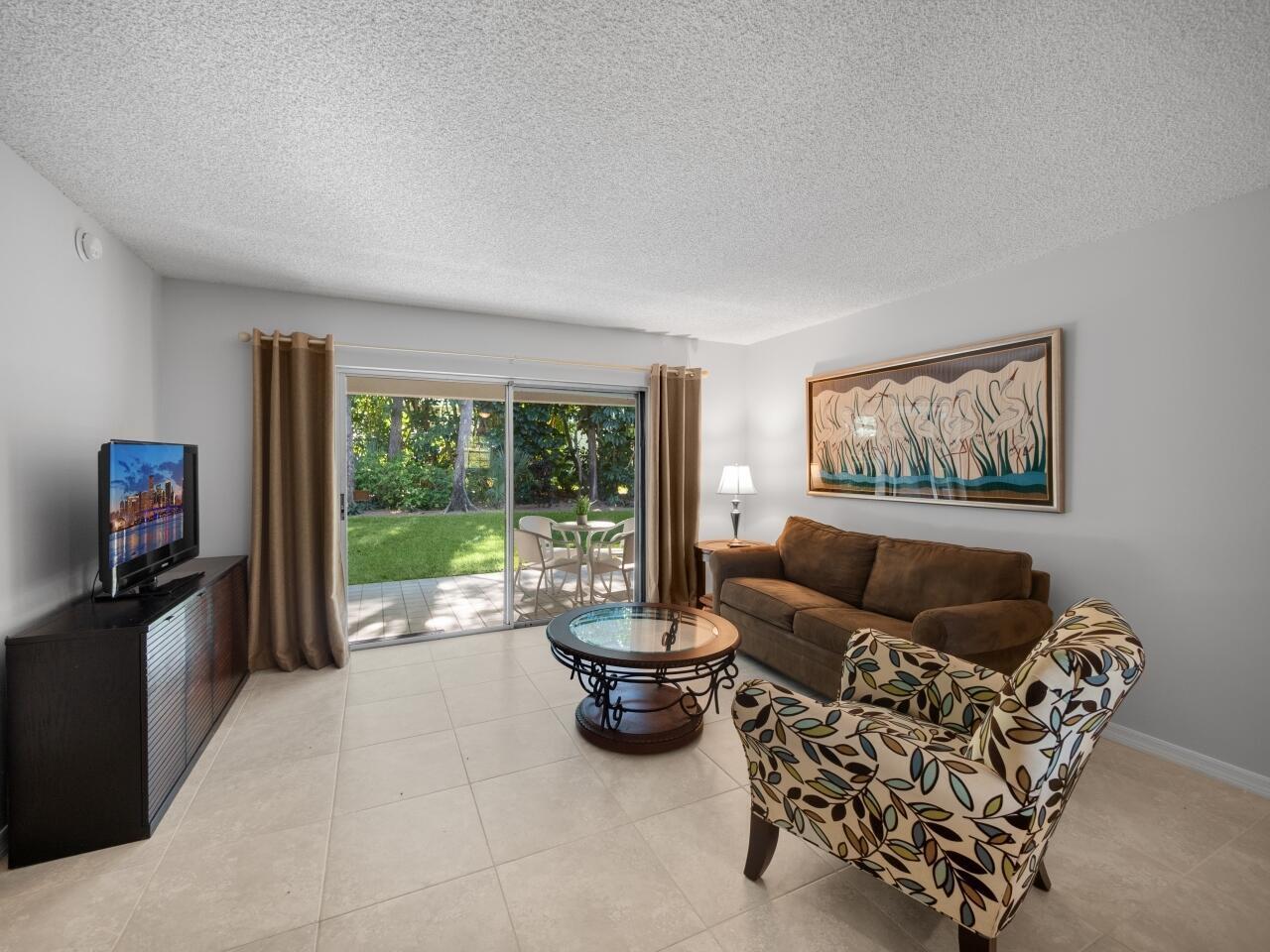 A living room with tile floors, a brown sofa, patterned armchair, and sliding glass doors — 1262 Sugar Sands Boulevard, West Palm Beach FL 33404, WEST PALM BEACH, FL