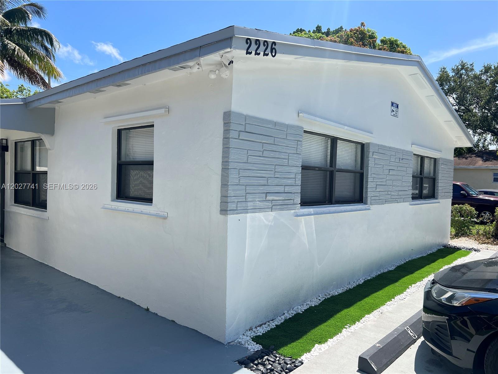 A white house exterior features grey stone accents, black-framed windows, and a small patch of turf — 2226 Cody St, Hollywood FL 33020, HOLLYWOOD, FL