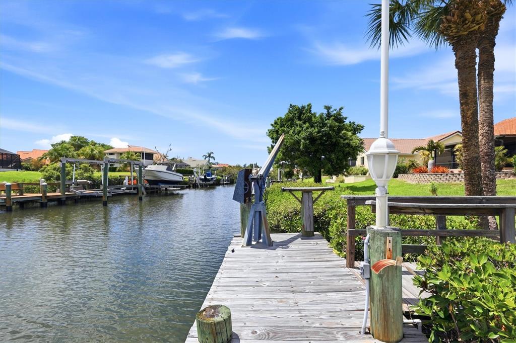 A wooden dock extends over a canal toward a boat lift and residential homes — 140 INLETS BOULEVARD UNIT 140, NOKOMIS, FL