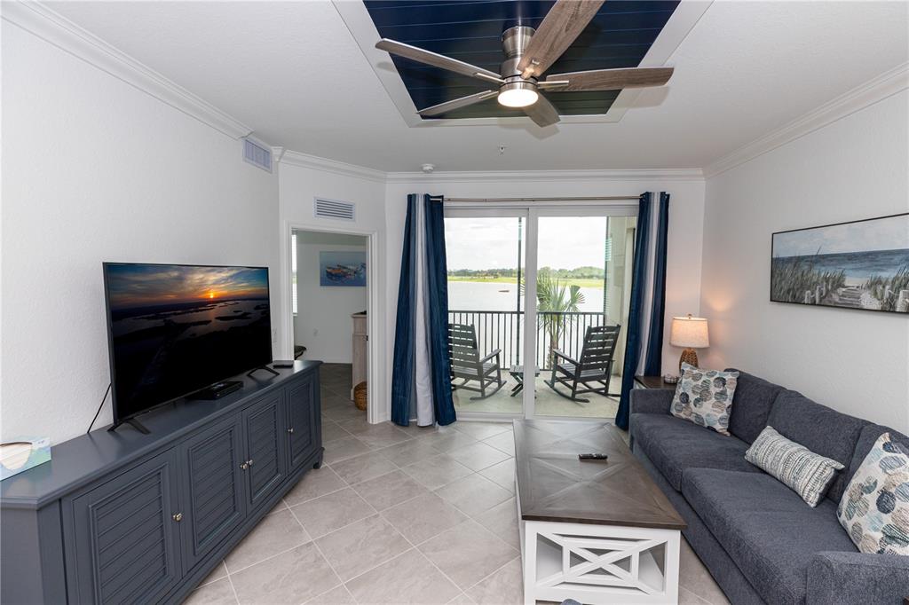 A living room features a blue media console, a gray sofa, and a balcony view — 15375 GREEN ACRES AVENUE UNIT 2228, PUNTA GORDA, FL