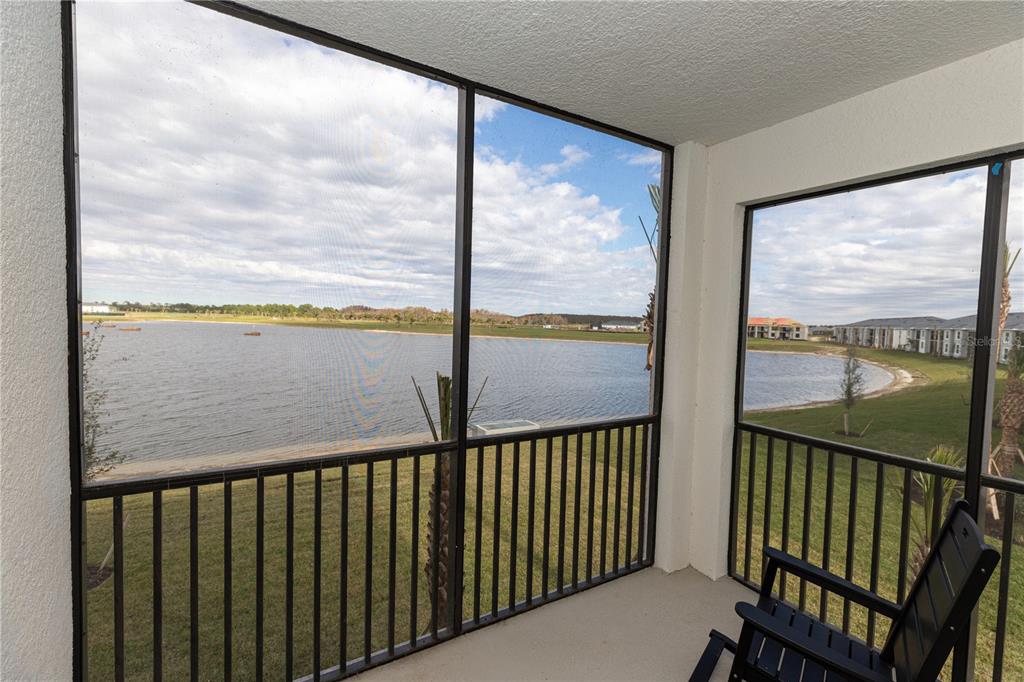 A screened-in balcony overlooks a large lake with grassy banks and distant buildings — 15375 GREEN ACRES AVENUE UNIT 2228, PUNTA GORDA, FL