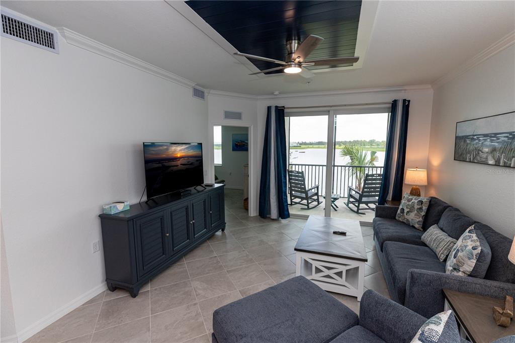 A living room features a dark blue media console, gray sofa, and a balcony view — 15375 GREEN ACRES AVENUE UNIT 2228, PUNTA GORDA, FL