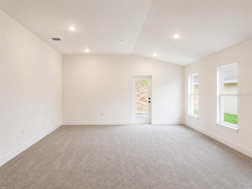 A bright, empty room features light-colored walls, gray carpeting, recessed lighting, and a glass-paneled door — 1643 ANN ROSE WAY, LEESBURG, FL