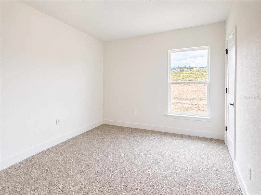 An empty bedroom features beige carpet, white walls, and a window overlooking a construction site — 1643 ANN ROSE WAY, LEESBURG, FL
