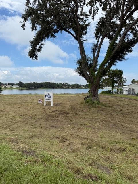 A vacant, grassy lot features a large tree and a real estate sign near water — 3131 SPIRIT LAKE ROAD, WINTER HAVEN, FL