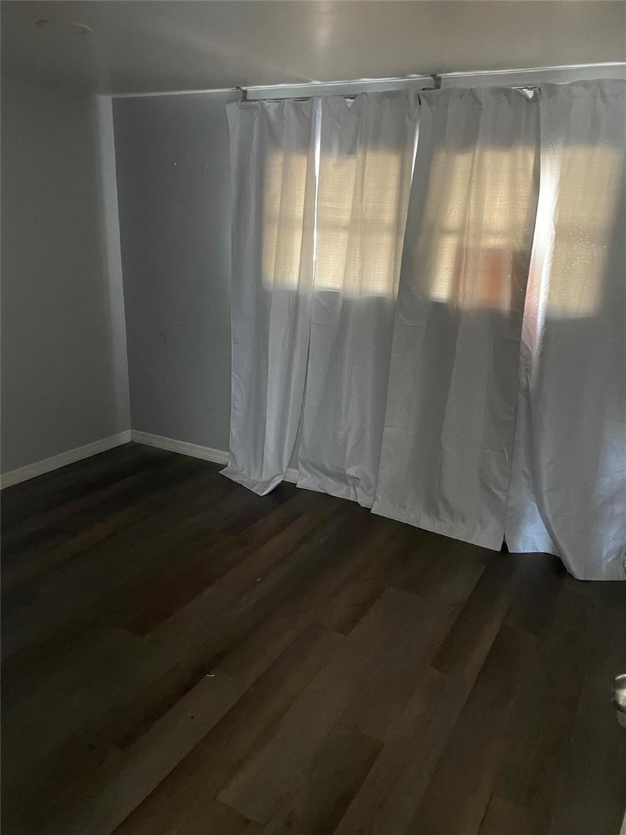 An empty room with dark wood-look flooring, gray walls, and white curtains over a window — 8508 SW 16th Court, Davie FL 33324, DAVIE, FL