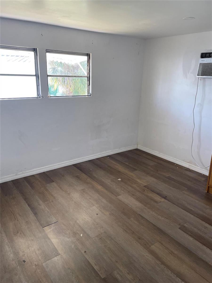 An empty room with light gray walls, wood-look flooring, two windows, and a wall-mounted air conditioner — 8508 SW 16th Court, Davie FL 33324, DAVIE, FL