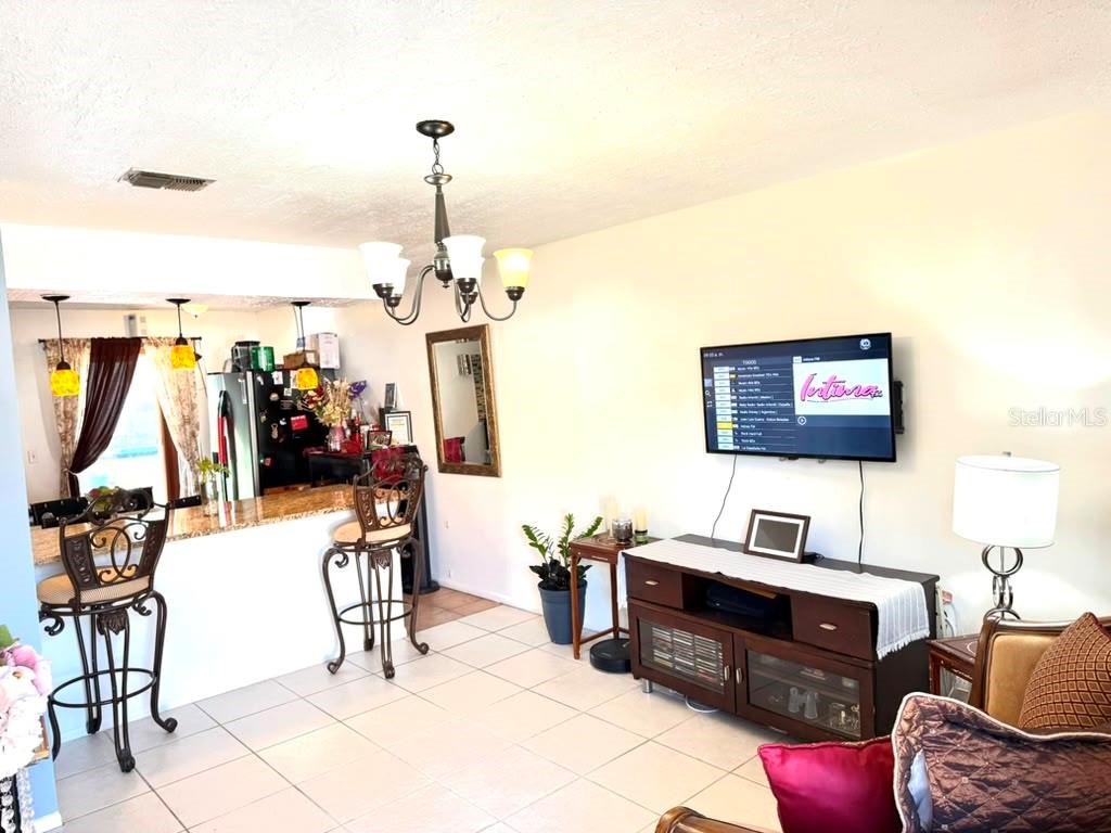 A living room with tile floors, a kitchen bar, and a wall-mounted television — 69 S MARBRISA WAY, KISSIMMEE, FL