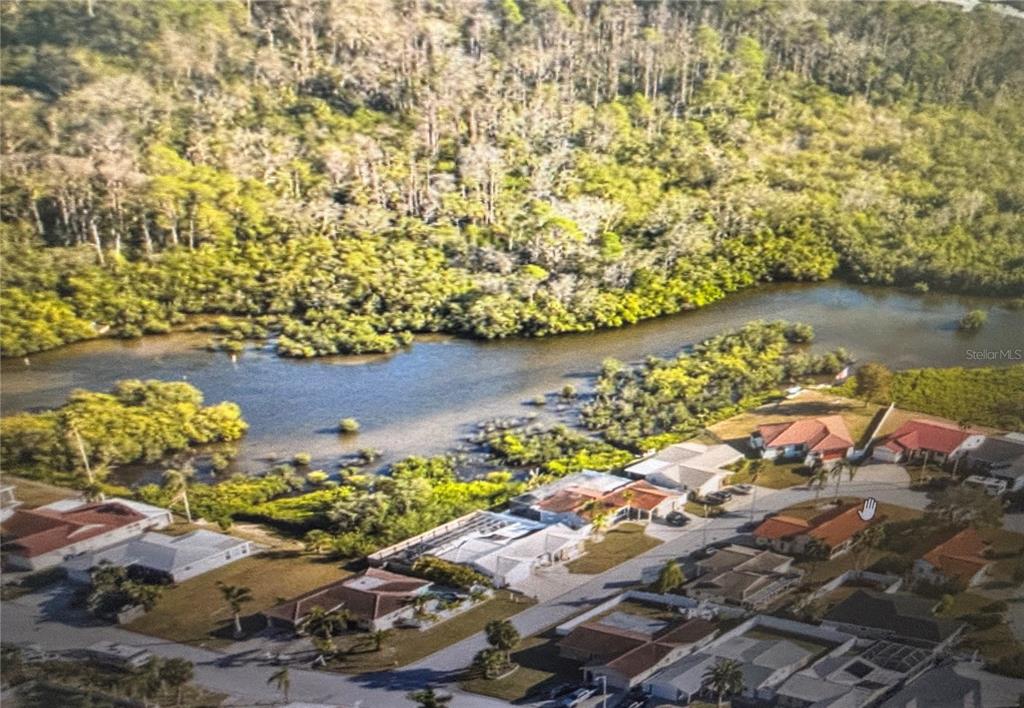 An aerial view shows a residential neighborhood situated along a wooded shoreline and waterway — 3982 RUDDER WAY, NEW PORT RICHEY, FL