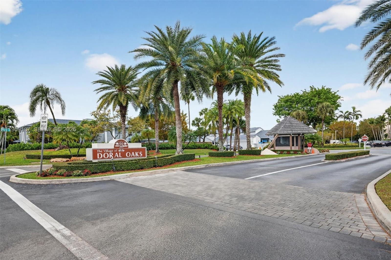 The entrance to The Village of Doral Oaks features a sign, palm trees, and guardhouse — 9725 NW 52nd St # 103, Doral FL 33178, DORAL, FL