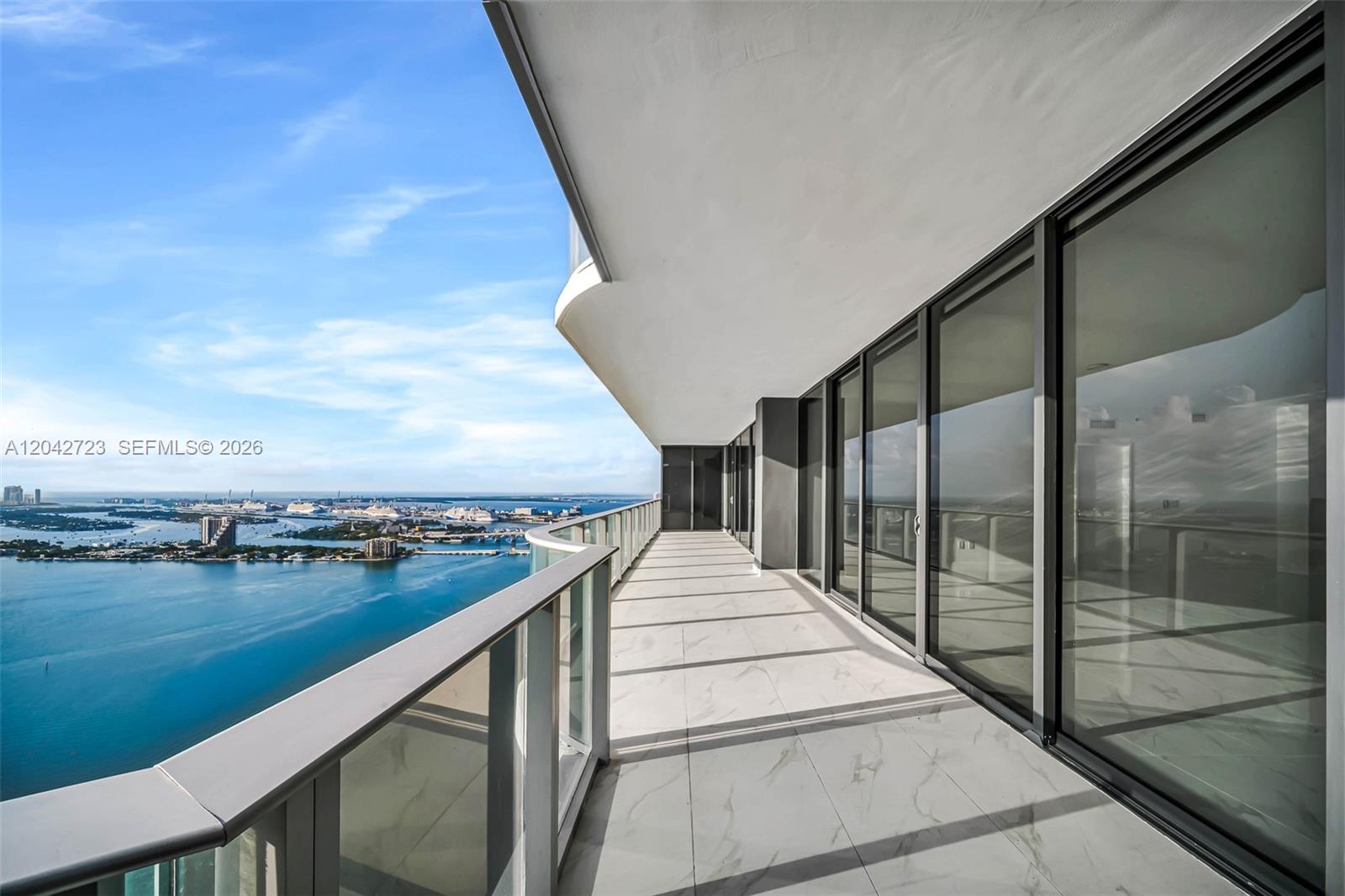 A high-rise balcony with marble-look tile flooring overlooks a bay with distant city views — 700 NE 24th St # 4702, Miami FL 33137, MIAMI, FL