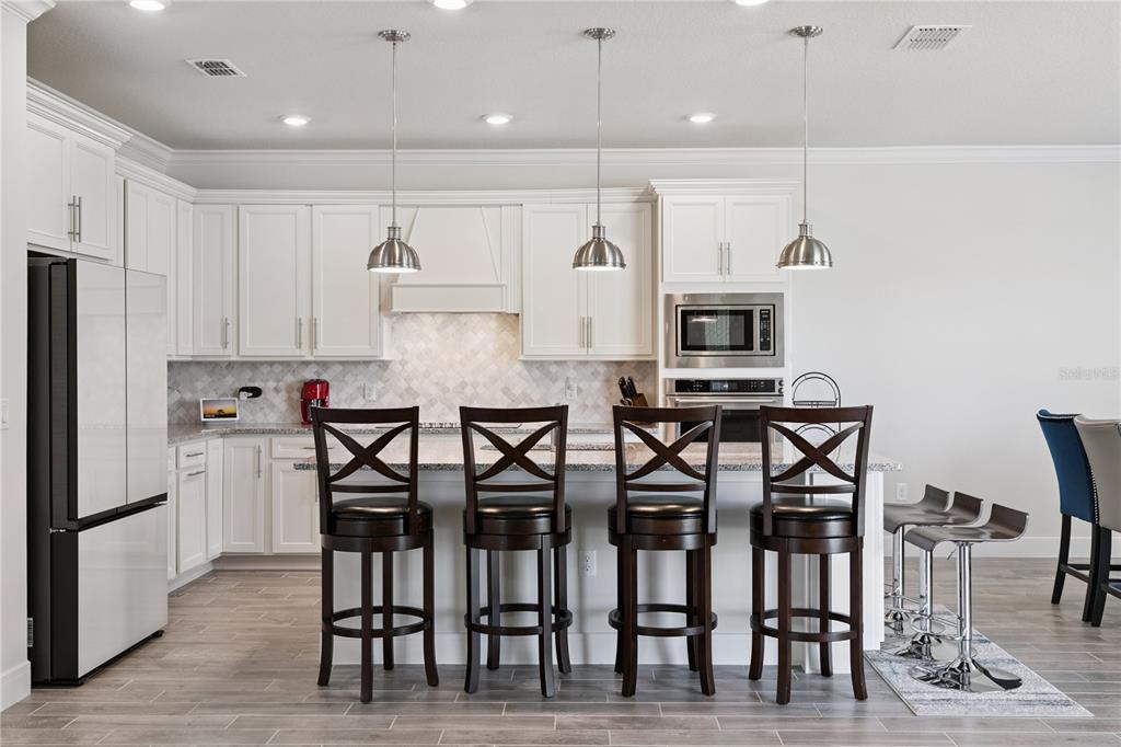 A kitchen features white cabinets, a central island with four barstools, and stainless steel appliances — 1462 GRAND PALM DRIVE, ORLANDO, FL