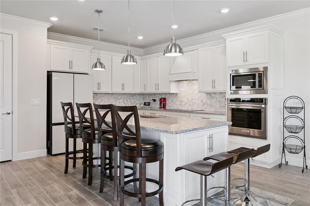 A modern kitchen features white cabinetry, a granite-topped island, stainless steel appliances, and bar stools — 1462 GRAND PALM DRIVE, ORLANDO, FL