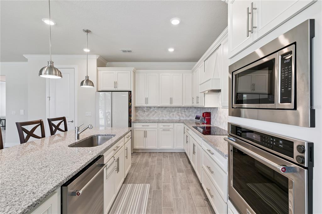 A modern kitchen features white cabinetry, granite countertops, stainless steel appliances, and tile flooring — 1462 GRAND PALM DRIVE, ORLANDO, FL