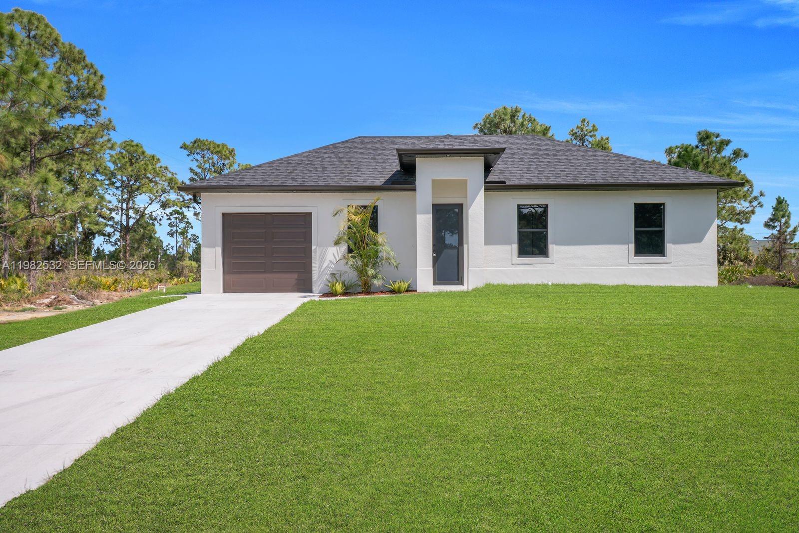 A single-story white house with a dark roof, a garage, and a front lawn — 635 Summit Ave S, Lehigh Acres FL 33974, LEHIGH ACRES, FL