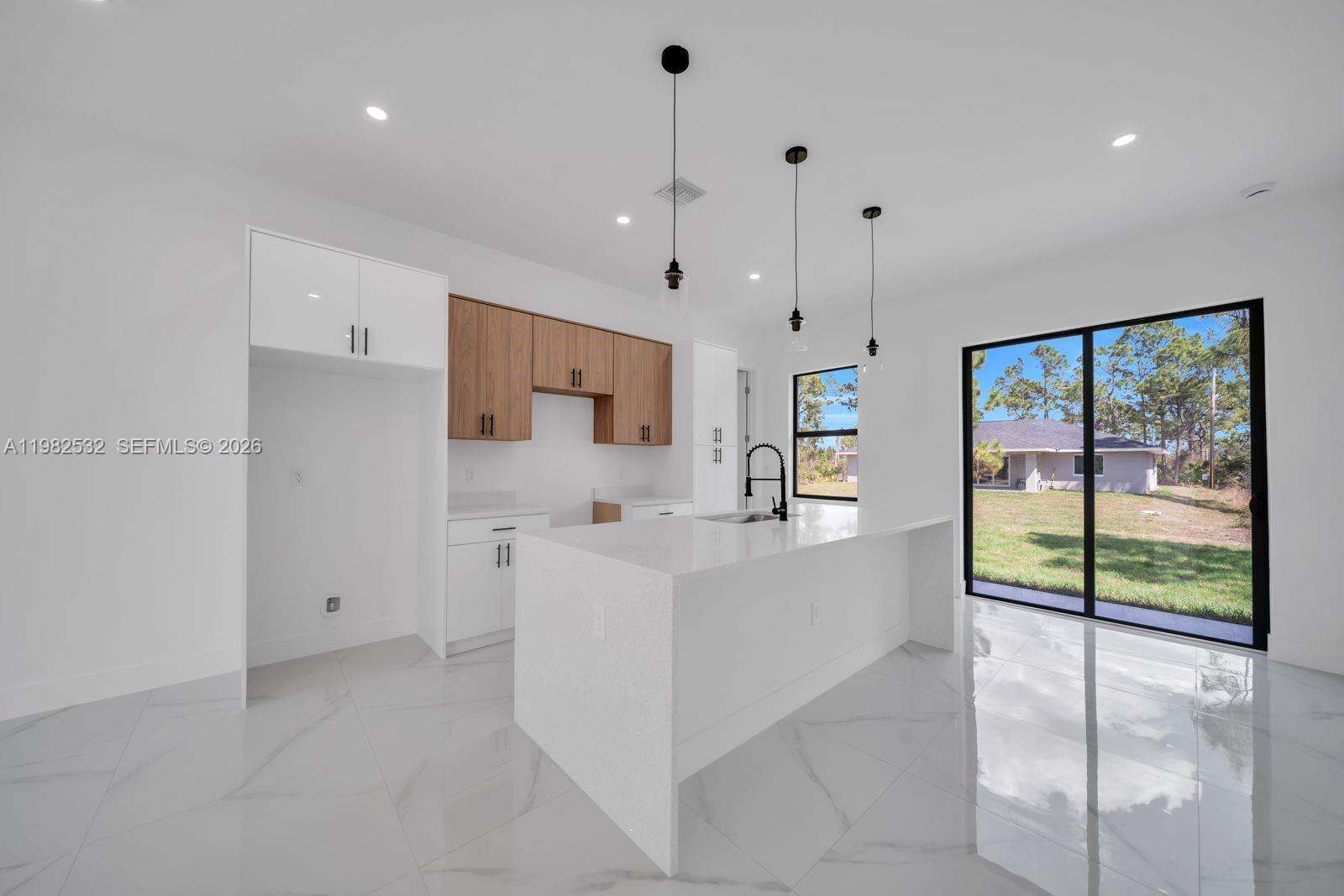 A modern kitchen features white cabinets, wood-toned upper cabinets, a quartz island, and tile flooring — 635 Summit Ave S, Lehigh Acres FL 33974, LEHIGH ACRES, FL