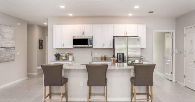 A kitchen features white cabinets, stainless steel appliances, a granite island, and three bar stools — 3 PORTER LANE, PALM COAST, FL