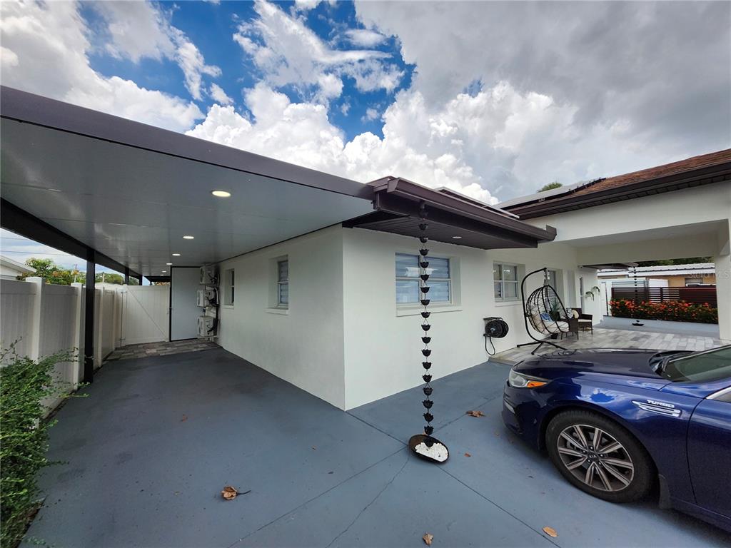 A blue car is parked under a carport next to a white house with a rain chain — 7514 PARADISE PLACE, TAMPA, FL