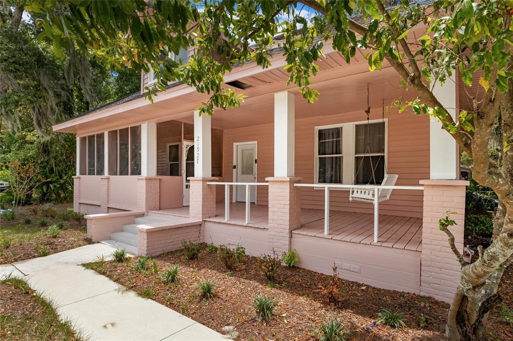 A pink house with a covered front porch, white railings, and a hanging porch swing — 21927 SE 69TH AVENUE, HAWTHORNE, FL