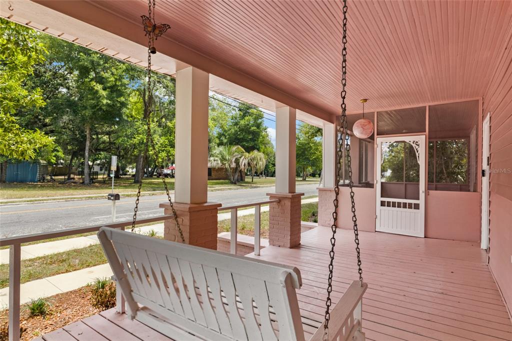 A pink-painted covered porch features a white wooden swing and a screened-in entryway — 21927 SE 69TH AVENUE, HAWTHORNE, FL