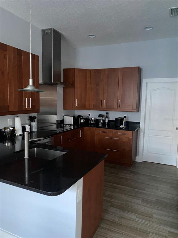 A kitchen features dark wood cabinets, black countertops, a stainless steel range hood, and flooring — 2251 NAIRN DRIVE, WINTER PARK, FL