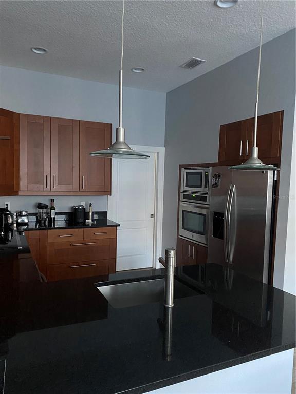 A kitchen features dark wood cabinets, black countertops, stainless steel appliances, and two pendant lights — 2251 NAIRN DRIVE, WINTER PARK, FL