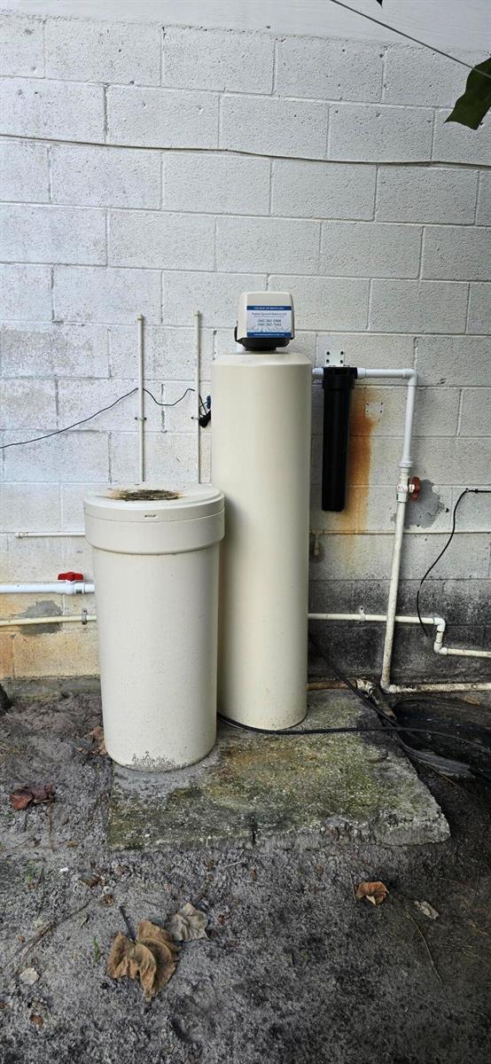 A water softener system with a brine tank and filter sits against an exterior block wall — 15720 Okeechobee Boulevard, FL 33470, FL