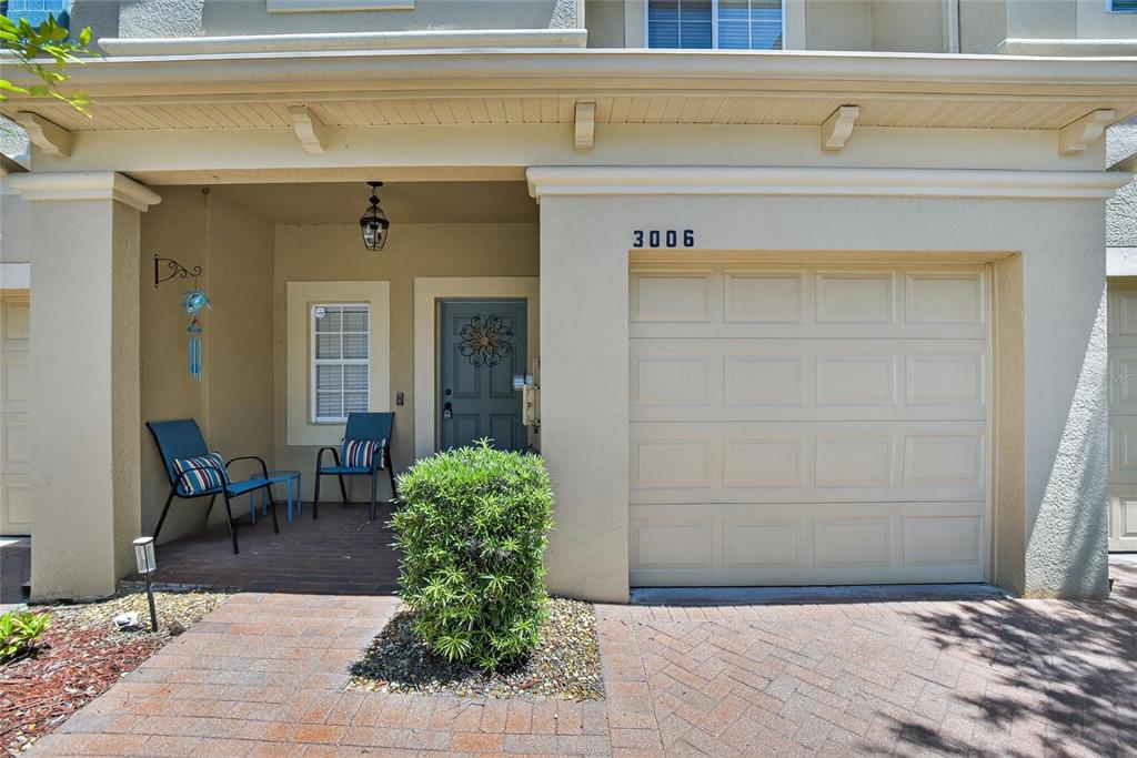 A beige townhouse exterior features a single-car garage, a covered porch, and a small bush — 3006 GIRVAN DRIVE, LAND O LAKES, FL