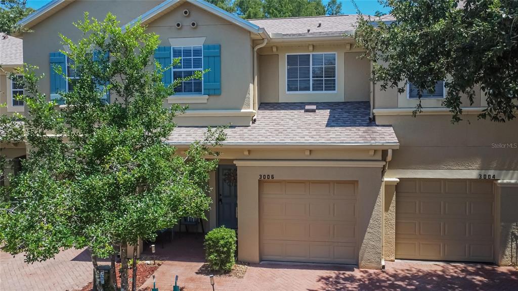 A two-story townhouse exterior features tan stucco walls, blue shutters, and two garage doors — 3006 GIRVAN DRIVE, LAND O LAKES, FL