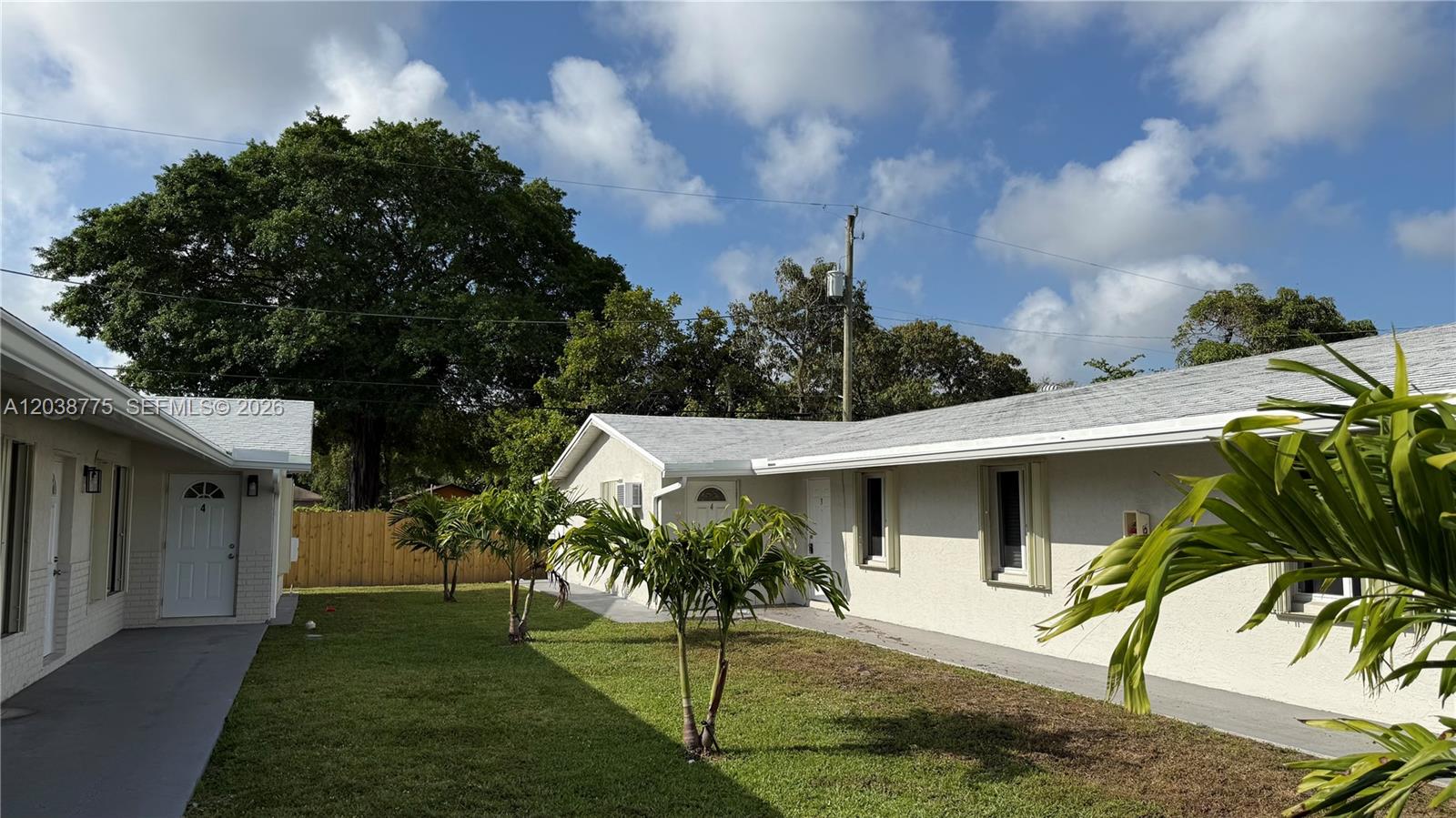 A grassy courtyard sits between two single-story residential buildings with white stucco walls — 220 NW 12th St # 4, Pompano Beach FL 33060, POMPANO BEACH, FL