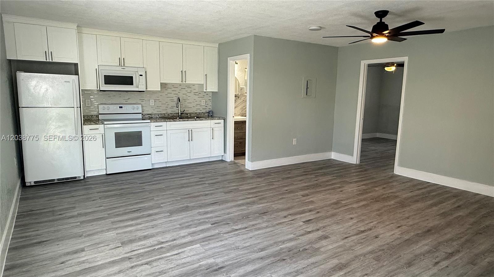 A kitchen with white cabinets and appliances opens into a living area with gray flooring — 220 NW 12th St # 4, Pompano Beach FL 33060, POMPANO BEACH, FL