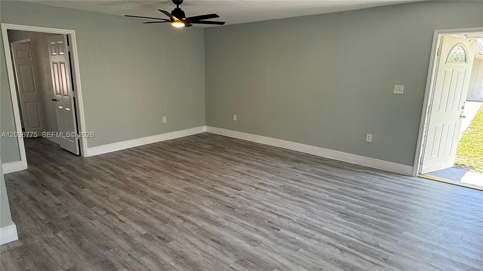 An empty room features light gray walls, wood-look flooring, a ceiling fan, and an exterior door — 220 NW 12th St # 4, Pompano Beach FL 33060, POMPANO BEACH, FL