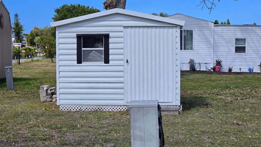 A white storage shed with a single window and a sliding door sits on grass — 1464 BLUE HERON DRIVE, ENGLEWOOD, FL
