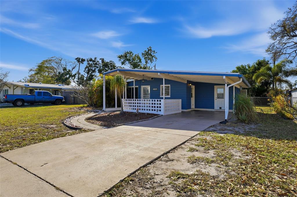 A blue single-story house features a concrete driveway, a carport, and a white lattice porch — 1904 31ST STREET W, BRADENTON, FL