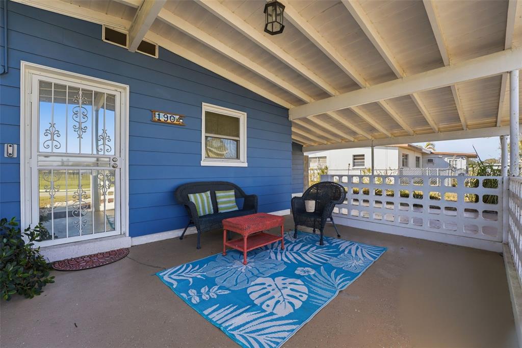 A blue house features a covered front porch with wicker furniture and a patterned rug — 1904 31ST STREET W, BRADENTON, FL