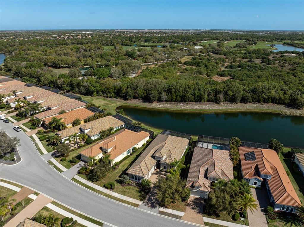 An aerial view shows a row of suburban houses bordering a pond and wooded area — 14911 CASTLE PARK TERRACE, LAKEWOOD RANCH, FL