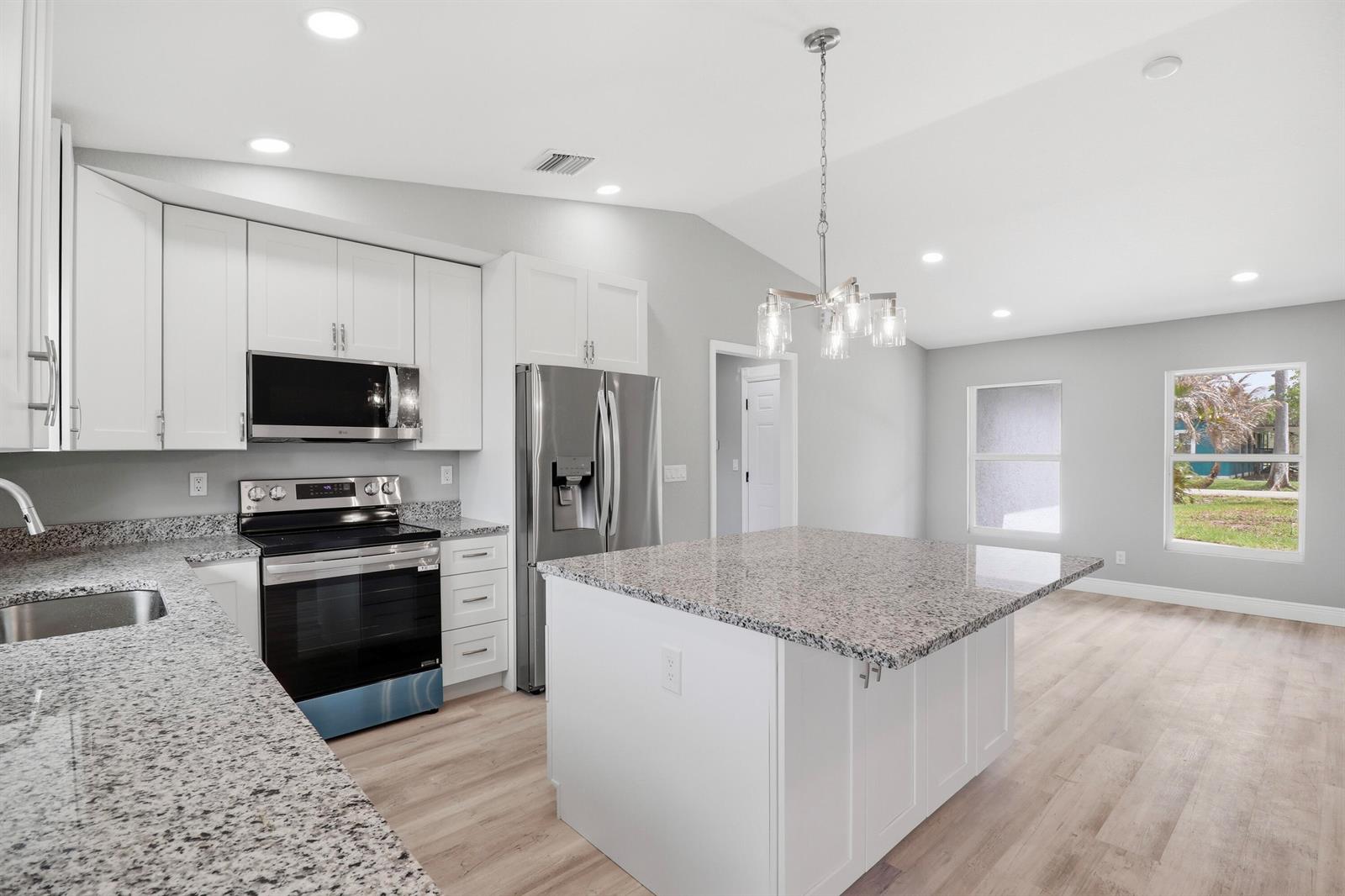 A modern kitchen features white cabinets, granite countertops, stainless steel appliances, and a central island — 2805 SE Carroll Street, Stuart FL 34997, STUART, FL