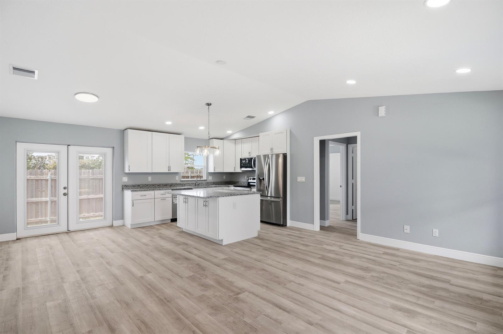 A kitchen with white cabinets, granite countertops, and an island opens to a living area — 2805 SE Carroll Street, Stuart FL 34997, STUART, FL
