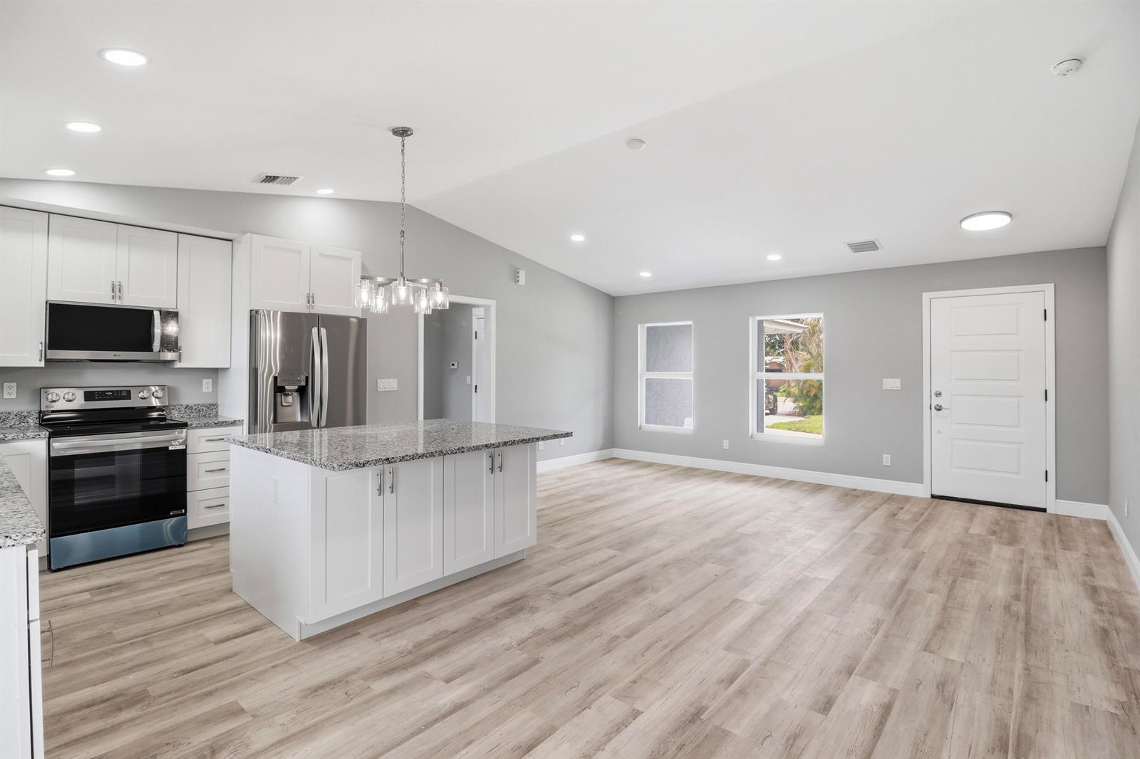 A modern kitchen features white cabinets, granite countertops, stainless steel appliances, and light wood flooring — 2805 SE Carroll Street, Stuart FL 34997, STUART, FL