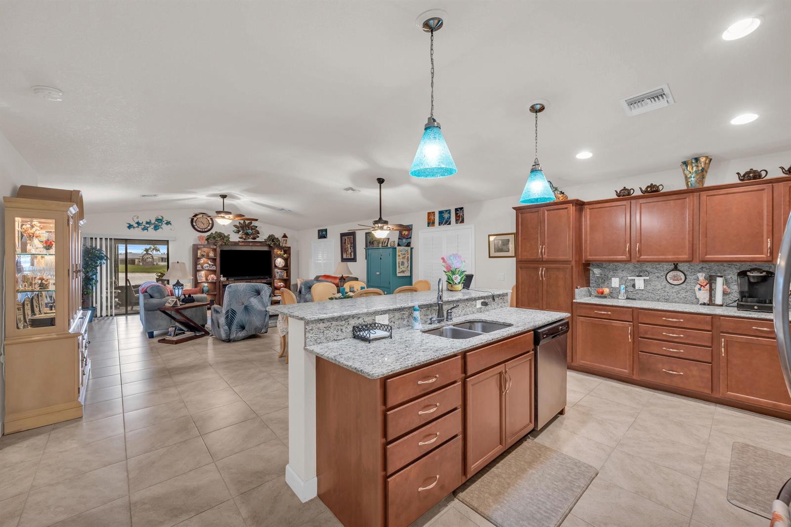 An open-concept kitchen with granite countertops and wood cabinets overlooks a living room area — 14961 Aguila, Fort Pierce FL 34951, FORT PIERCE, FL
