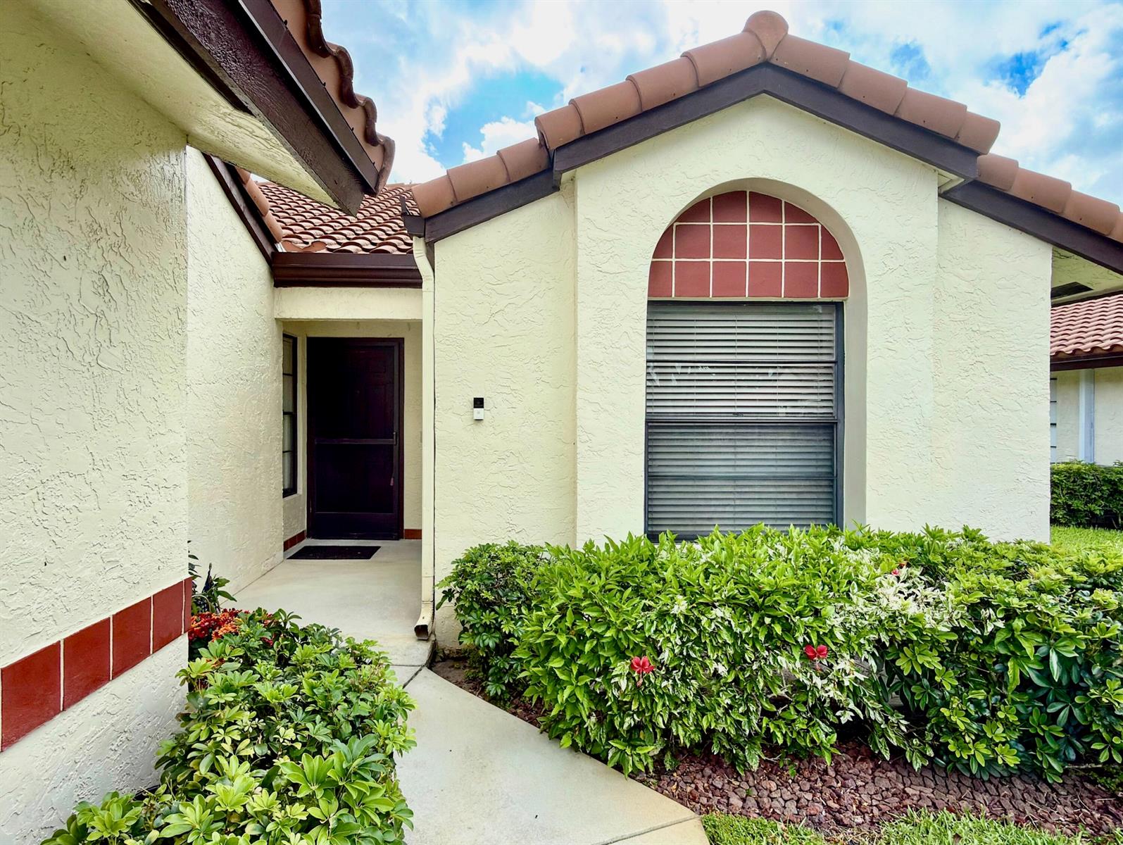 A beige stucco house exterior features a brown tiled roof, arched window, and front entryway — 10975 Dolphin Palm Court # B, Boynton Beach FL 33437, BOYNTON BEACH, FL
