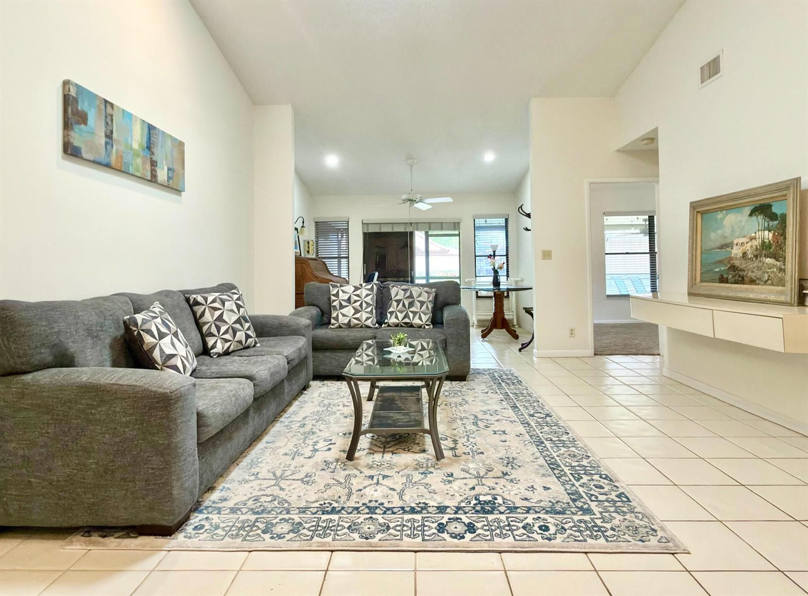 A living room features gray sofas, a glass coffee table, and a patterned area rug — 10975 Dolphin Palm Court # B, Boynton Beach FL 33437, BOYNTON BEACH, FL