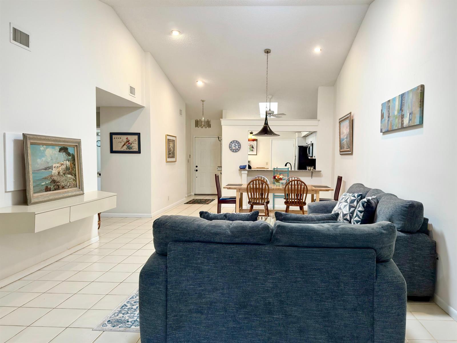 A living room with a blue sofa, dining area, and tiled floors under vaulted ceilings — 10975 Dolphin Palm Court # B, Boynton Beach FL 33437, BOYNTON BEACH, FL