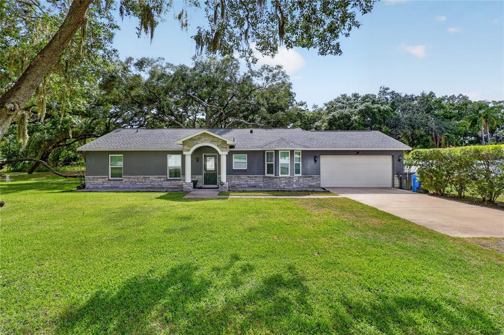 A single-story house with gray siding, stone accents, and a two-car garage — 7608 COPELAND ROAD, ODESSA, FL