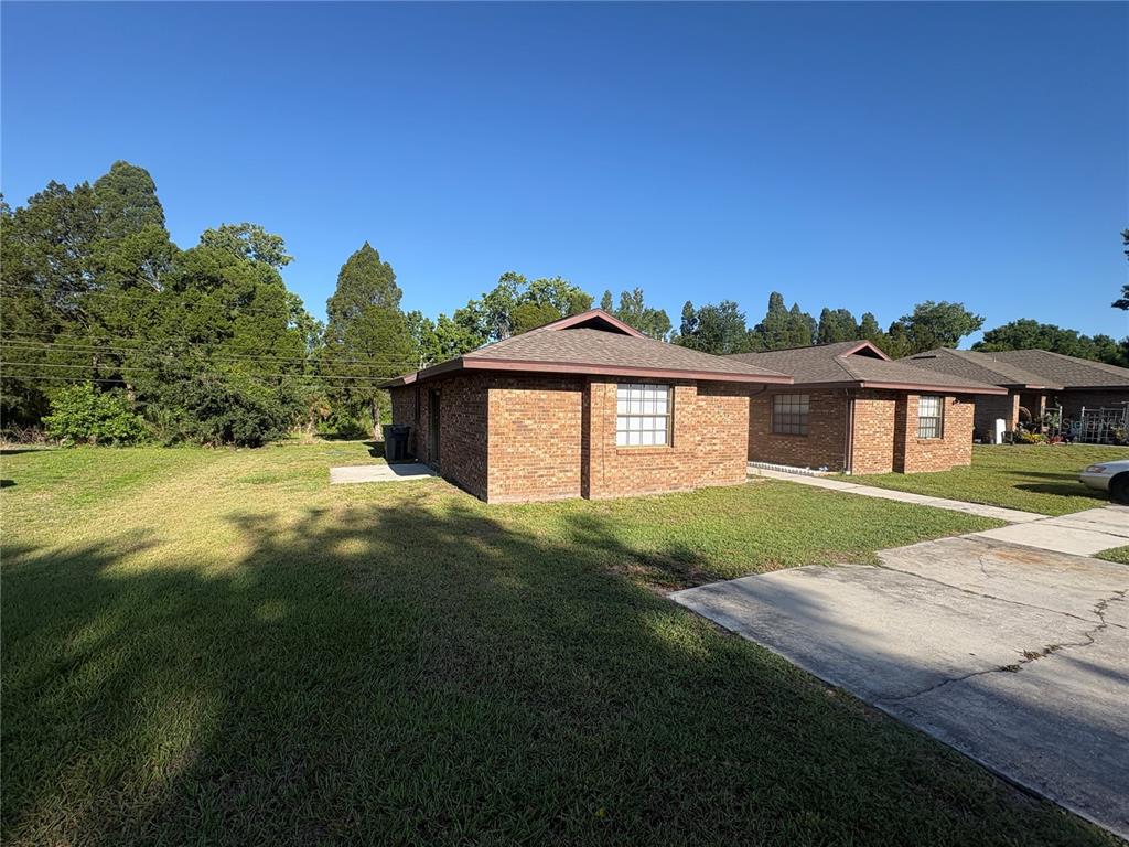 A side view of a single-story brick duplex with a concrete driveway and grassy yard — 3122 JULIA COURT, LAKELAND, FL