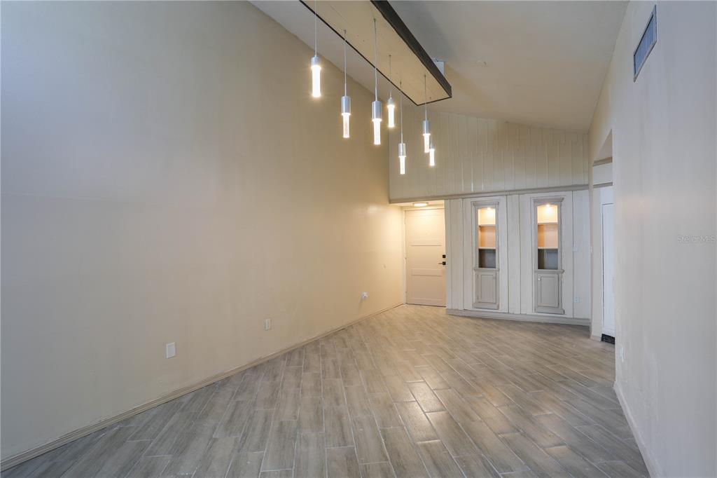 An empty room features wood-look tile flooring, a vaulted ceiling, and a modern pendant light fixture — 3655 ATRIUM DRIVE UNIT 2, ORLANDO, FL